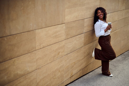 African American Woman Leaning on Urban Wall Holding Coffee Smiling Confident Casual Business Lifestyle Portrait