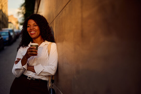 Smiling African American Woman With Coffee Leaning On City Wall for Casual Business and Urban Lifestyle