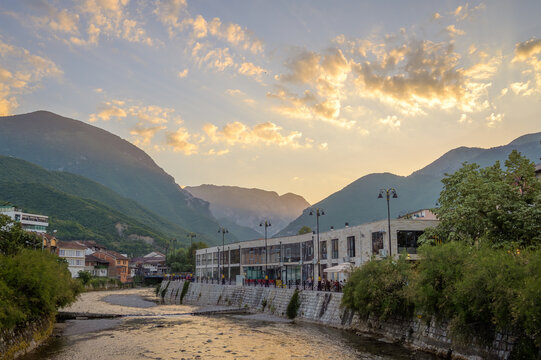 Peja, Kosovo - June 28, 2026: Riverside promenade along the Lumbardhi River with restaurants and dramatic mountain landscape during sunset in Peja, Kosovo.