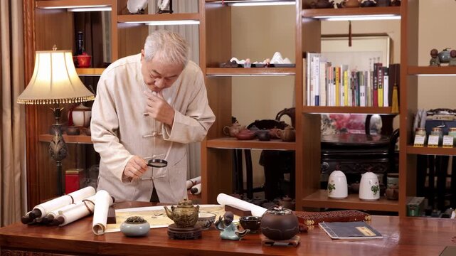 Senior man hands holding magnifying glass to exploring reference checks ancient scrolls using magnifying glass appraising historical portrait pictures on wooden table surrounded by vintage documents