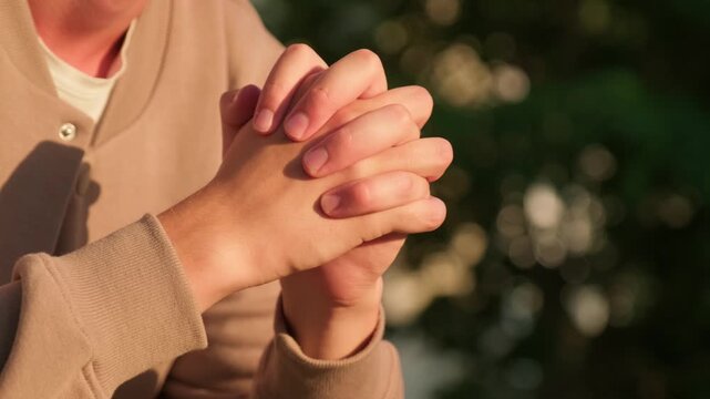 Anxious man with a nervous hand gesture. Close up of a man sitting outdoors with his fingers and hands clasped together.