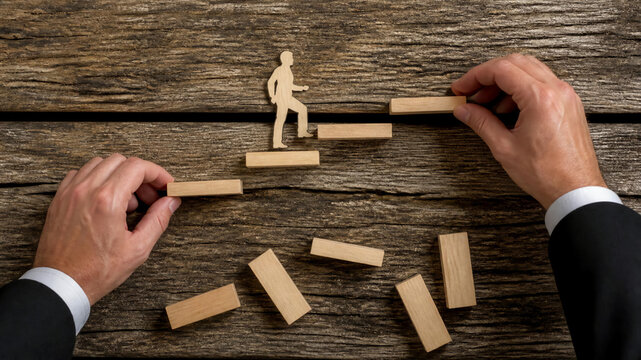 A businessman's hands build a wooden staircase for a paper cutout figure, symbolizing professional growth, career development, and strategic success on a rustic textured background.