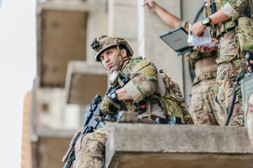 Obraz premium Military tactical team reviews mission plan on rugged laptop during outdoor field briefing