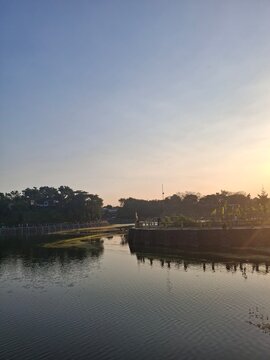 Warm sunset colors are mirrored vividly on the clear water surface of Tambak Boyo, creating a serene and glowing composition. Perfect for concepts related to travel, nature, and Indonesian landscapes.