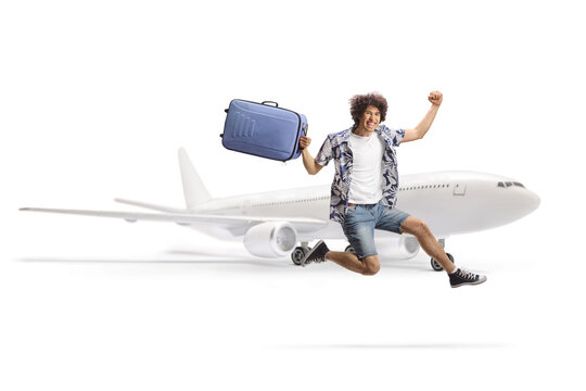 Happy male traveler jumping with a suitcase in front of a plane