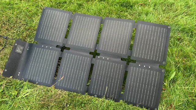 Portable foldable solar panels on grass generating clean renewable energy. Concept of off-grid power, sustainable technology, camping, eco-friendly travel and portable electricity.