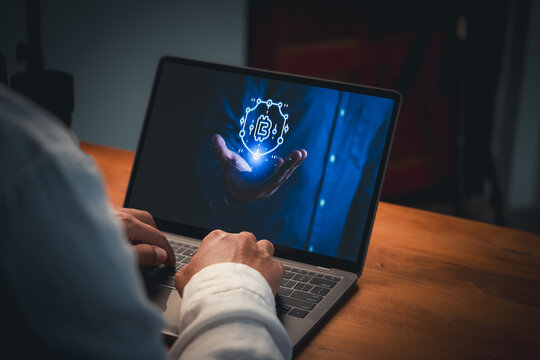 Person typing on laptop displaying a glowing blue hologram of a hand holding a shield with cryptocurrency symbol. Concept of blockchain security, safe digital investment and crypto wallet.