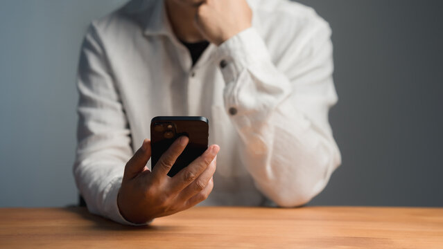 Modern smartphone technology concept. Serious adult man thinking while holding a mobile phone in a home office. Online shopping, customer service and payment.