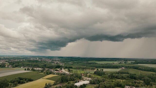 Aerial drone shot slowly flying toward a dramatic arcus shelf cloud over a small rural village, with moody overcast fields creating a cinematic countryside landscape.