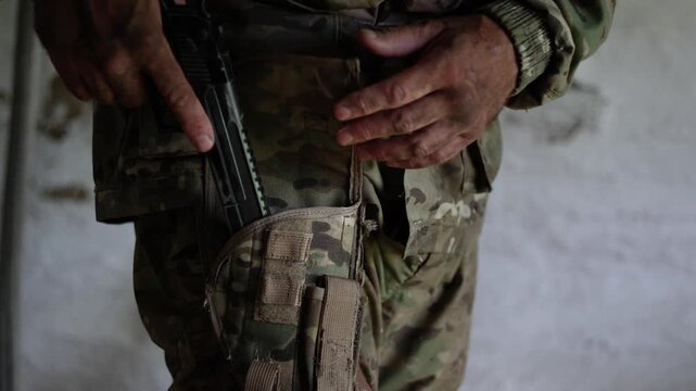 A close-up of a soldier's hand pulling a pistol from its holster and cocking the hammer. A tense situation in a combat zone. Slow motion 4K footage.