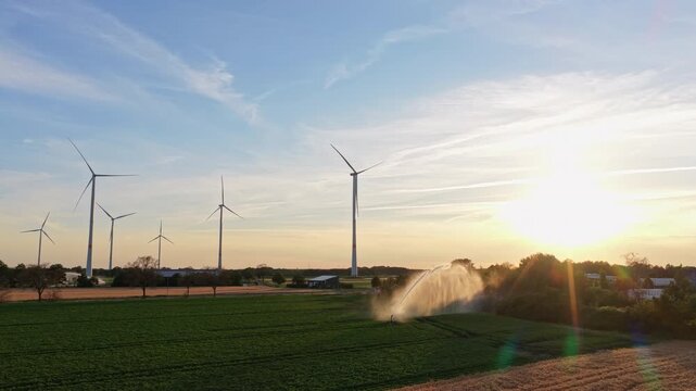 Wind turbines farm. Green energy. Sprinkler irrigation system watering field. Wind mill for renewable electric energy production. Irrigation system and windmill in rural area. Agriculture irrigation