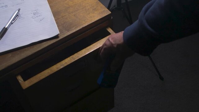 Adult hand opens a wooden desk drawer under handwritten notes and pulls out a small blue calculator.