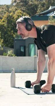 Weights, headphones and man outdoor for push up workout, muscle or body building with music. Audio tech, playlist and mature person with dumbbells for arm exercise, health or active in backyard.