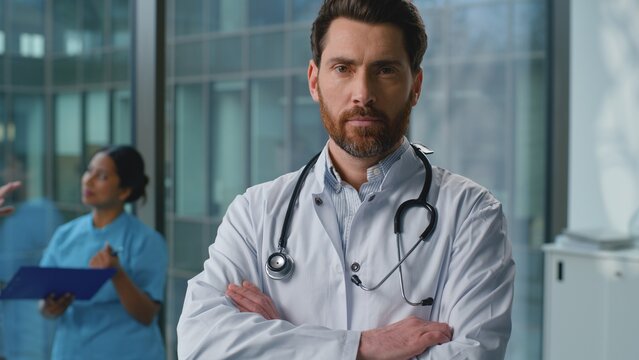Portrait serious confident Caucasian man doctor posing with crossed hands in hospital. Authority male therapist in white medical uniform looking at camera crossing arms working in laboratory clinic