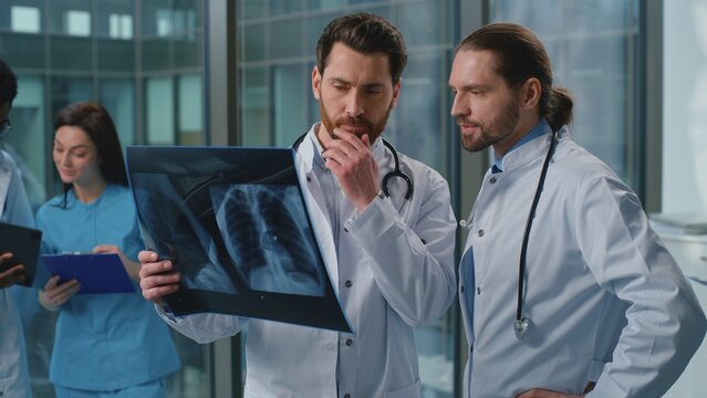Two Caucasian men doctors discussing x-ray of lungs talking males radiologist and physician holding scan radiography discussing health diagnosis talk diagnostic teamwork at medicine hospital clinic