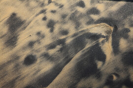 Abstract patterns of black and golden beach sand shaped by wind and waves, creating a striking natural texture and coastal background.