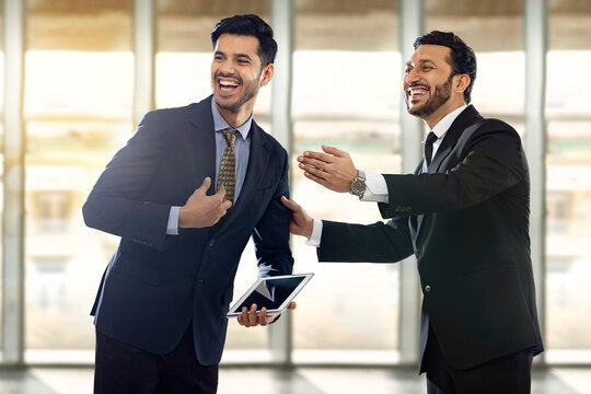 Two corporate employees in formal business suit laughing with one of them selected and the other appreciating.