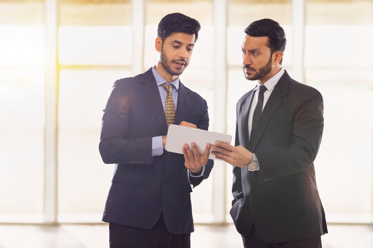 Corporate employees in formal business suit working together on a digital tablet with one of them looking sideways.