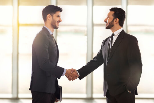 Corporate employees in formal business standing together in office shaking hands.