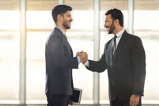 Corporate employees in formal business standing together in office while holding each other's hand with firm grip.