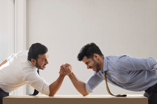 Corporate employees in formal clothing engaged in an arm wrestling match.