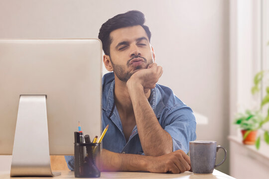 A corporate employee in formal clothing pouting behind his desktop at workdesk.