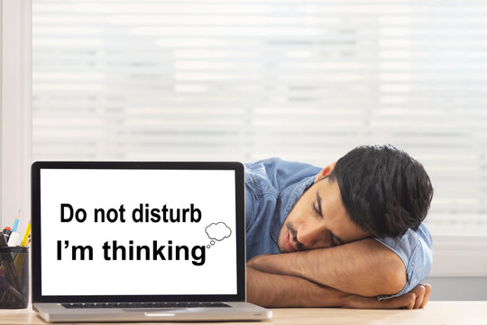 An employee sleeping behind a laptop screen displaying DND at his workdesk.