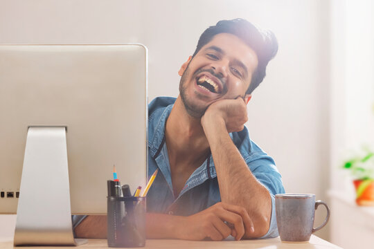 A corporate employee in formal clothing smiling behind his desktop at workdesk.