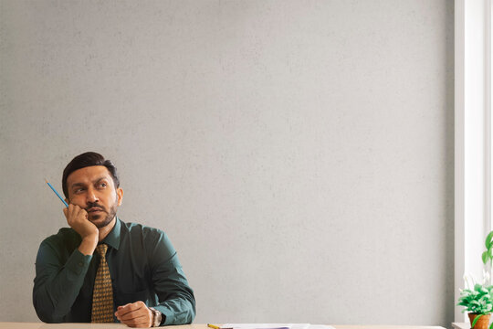 A corporate employee in formal clothing holding a pencil thinking something.