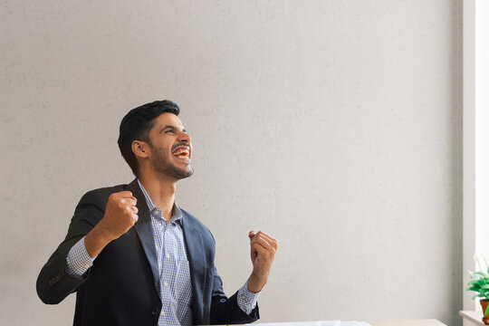 Portrait of a corporate employee in formal business suit clenching fists to celebrate his success.