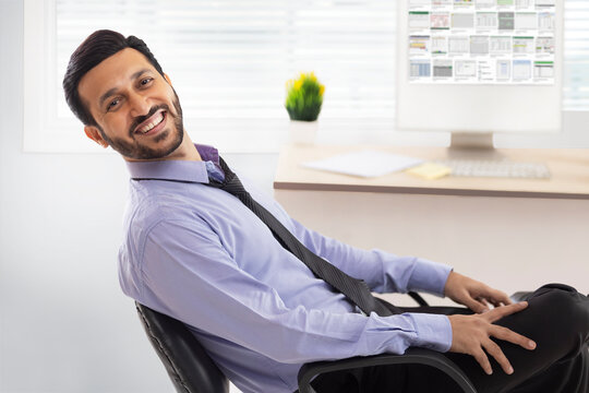 A corporate employee sitting in formal clothing smiling at his workdesk.