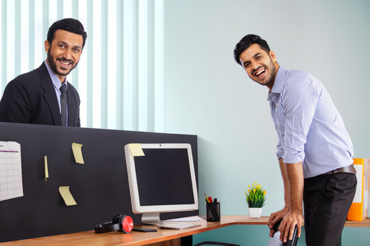 Corporate employees in formal clothing standing and smiling at workdesk.