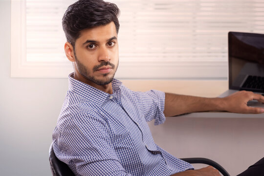 A corporate employee in formal clothing sitting at his workdesk looking at camera.