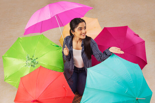 Portrait of a young girl kneeling with surrounded with multicolored umbrellas  