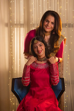 Young girl sitting on chair and mother holding her from backside