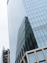 Obraz premium Modern Glass Office Skyscraper with Reflective Facade in Financial District, Contemporary Corporate Architecture, Urban Business Tower Viewed from Street Level Against Bright Sky