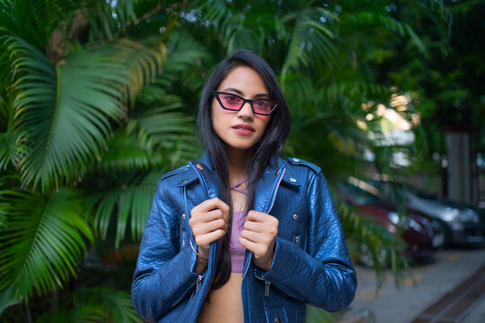 A young woman standing outside wearing a crop top and leather jacket.