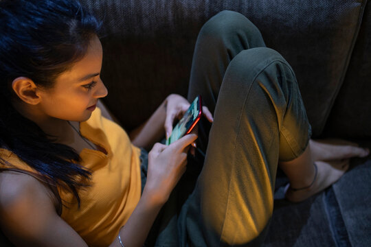 A young woman sitting alone in her room browsing social media on her mobile phone .