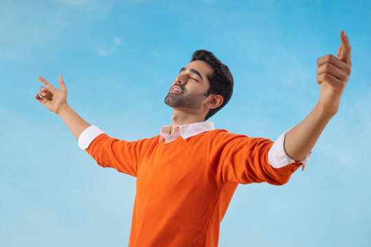 Happy man standing under the blue sky with his arms outstretched and eyes closed