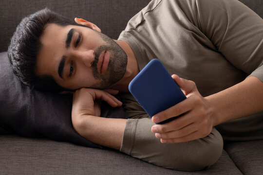 Portrait of a young man lying on sofa and looking at the Smartphone