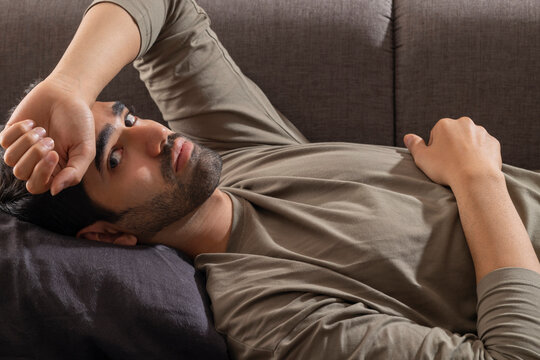 Portrait of a young man looking at the camera while lying on sofa