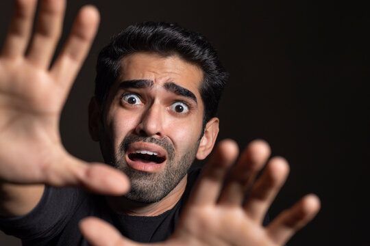 Portrait of a frightened young man looking at the camera and gesturing with his hands