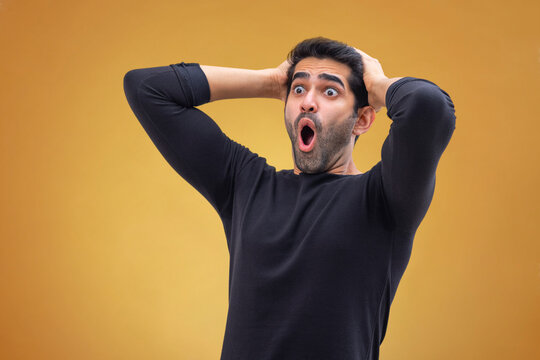 Portrait of a stunned young man with wide eyes,hands on his head and looking elsewhere with open mouth