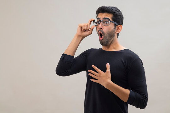Portrait of a stunned young man looking elsewhere with open mouth,wide eyes and hands on his chest 
