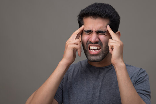 Portrait of a young man suffering from headache with hands on forehead 