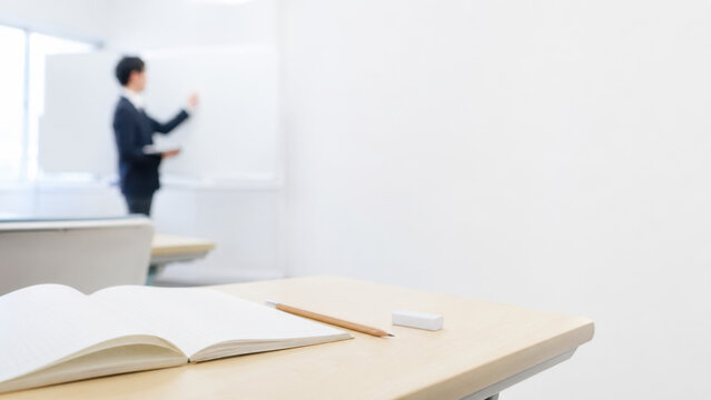 授業をする講師と机に置かれたノートと鉛筆のある教室