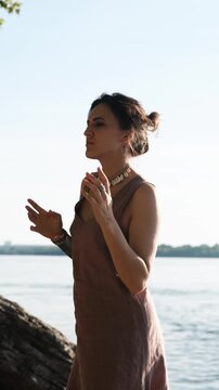 A beautiful brunette in boho style meditates and dances against the backdrop of a river on a sunny summer day. A magical ritual of relaxation unfolds.
