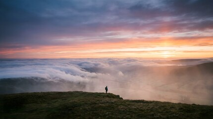Fototapeta premium Person standing on mountain peak at sunset. Hiker watching clouds over a misty valley.