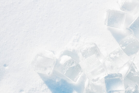 Crystal clear ice cubes on a natural snowy surface. Light blue tones background.