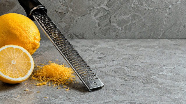 Fresh lemon and grated zest with a stainless steel zester on a grey stone countertop. Culinary food preparation background. Copy space for text